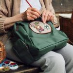 Grandmother sitting on bench sewing a patch on a black backpack