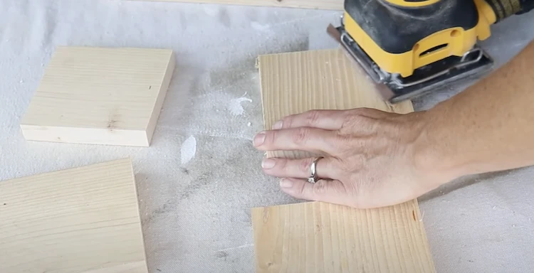 Crafter using electric sander to smooth surface of a plank of wood.