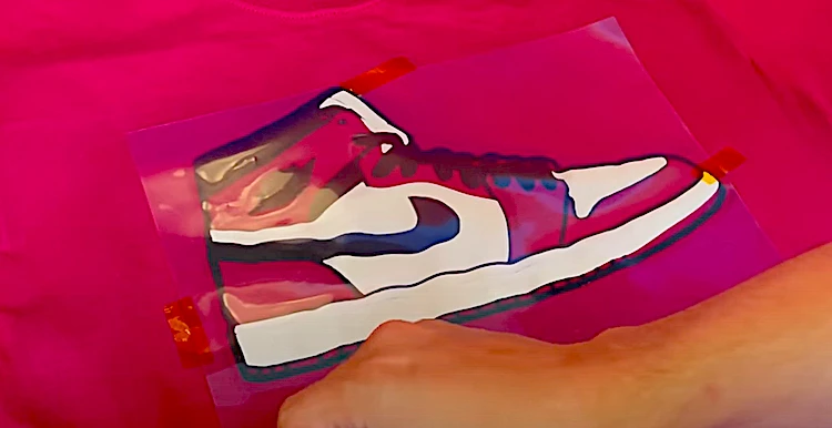 Artist aligning illustration of Nike Jordans on red cotton t-shirt just before the transfer process.