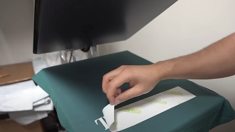 Heat press using heat and pressure to transfer design onto green t-shirt.