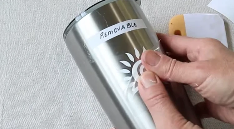 Arts & crafts person applying removable vinyl on metallic tumbler after cleaning surface with alcohol