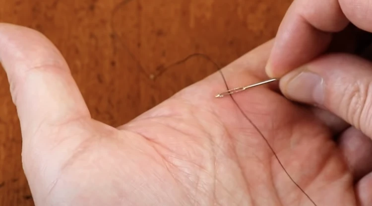 Man about to thread a needle by rubbing the eye of the needle along the thread.