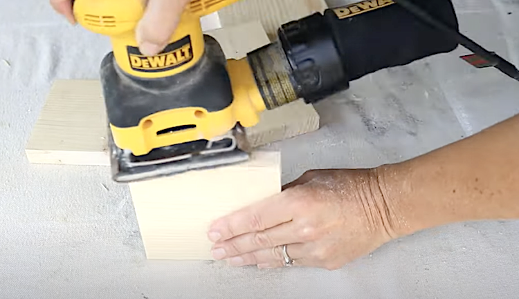 Crafter once again sanding down a plank of wood, but this time smoothing out the edges.